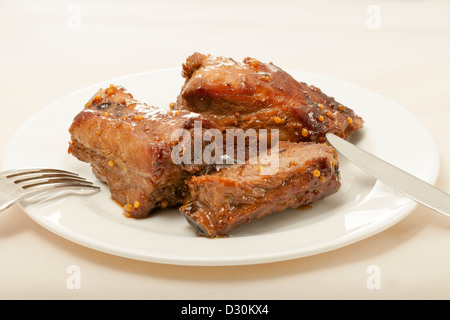 Spareribs in Senf-Honig-Sauce gekocht. Auf weißen Teller mit Messer und Gabel. Stockfoto