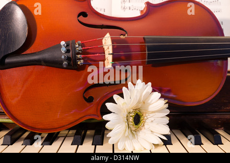 Eine Geige und eine weiße Blume sitzen auf einem Klavier Keyboard mit Noten im Hintergrund Stockfoto