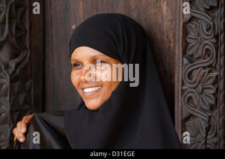 Swahili-Frau steht an einer traditionellen Zanzibar-Tür in der alten Festung, Lamu, Lamu Archipel, Kenia Stockfoto