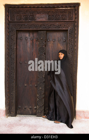 Swahili-Frau steht an einer traditionellen Zanzibar-Tür in der alten Festung, Lamu, Lamu Archipel, Kenia Stockfoto