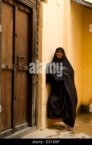 Swahili-Frau steht an einer traditionellen Zanzibar-Tür in der alten Festung, Lamu, Lamu Archipel, Kenia Stockfoto