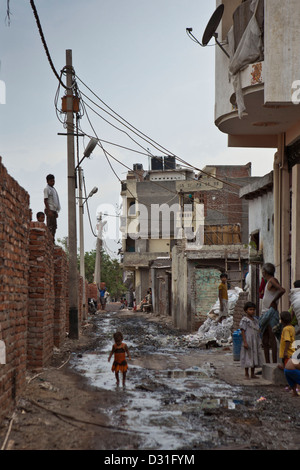 Armut leben in Tehkhand Slum, Delhi, Indien. Ein Kind geht durch offene Kanalisation Stream Häuser. Stockfoto