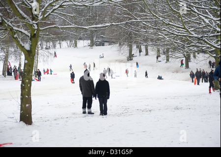 Eine große Anzahl von Menschen, Schlittenfahren oder Rodeln im Schnee bedeckt Landschaft mit zwei Erwachsenen im Vordergrund, die Hand in Hand. Stockfoto