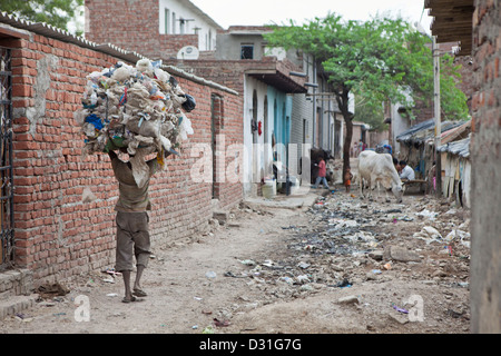 Armut leben in Tehkhand Slum, Delhi, Indien. Ein Mann trägt eine große Last von geborgenen Abfallmaterial auf seinem Kopf. Stockfoto