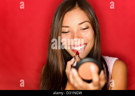 Schöne junge Mischlinge asiatischen / Caucasian Frau roten Lippenstift anwenden, während der Suche in Taschenspiegel auf rotem Grund Stockfoto