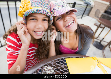 Lächelnde Mädchen tragen Hüte am Tisch Stockfoto