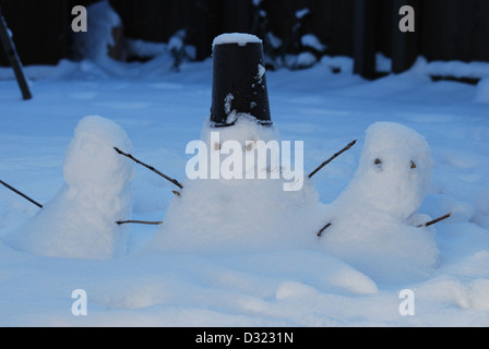 drei kleine Schneemänner im Schnee als es dunkel wird von Kindern mit einem Eimer für einen Hut gemacht und für Arme Stöcken und Steinen für Augen Stockfoto