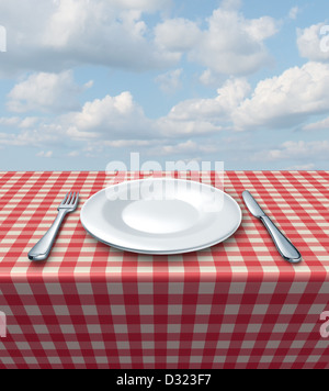 Gedeck mit einer Gabel Messer und weißen leeren Teller auf einer karierten rote und weiße Tischdecke auf einen blauen Sommerhimmel als Food-Service und klassische Restaurant-Symbol und Picknick Essen. Stockfoto