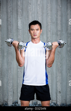 Sportlicher junge chinesische Mann mit Hanteln trainieren. Muskulöser asiatischen Mann mit Kraftgeräten trainieren. Stockfoto
