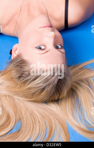 Eine schöne junge Frau, die Verlegung im Rückblick auf die Kamera gedreht im Studio auf blauem Hintergrund Stockfoto