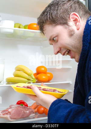 Gut aussehender Mann Essen Schinken Scheibe in der Nähe von offenen Kühlschrank Stockfoto