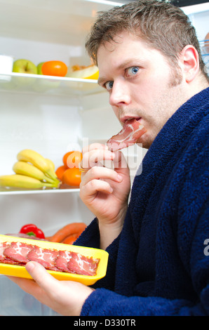 Gut aussehender Mann Essen Schinken Scheibe in der Nähe von offenen Kühlschrank Stockfoto