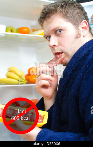 Gut aussehender Mann Essen Schinken Scheibe in der Nähe von offenen Kühlschrank Stockfoto