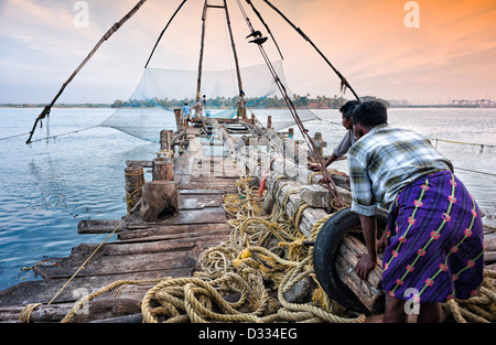 Fischer sind ein altes chinesisches Fischernetz im Hafen von Fort Kochi, Kerala, Indien an einem späten Nachmittag im Winter. Stockfoto