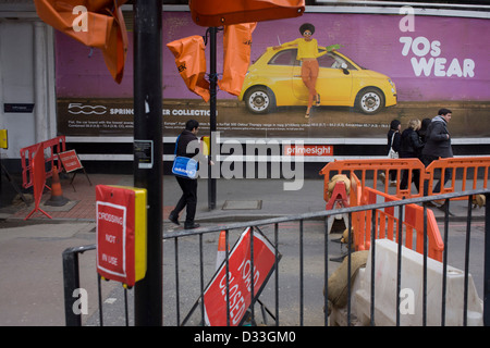 Fußgänger laufen unter einem breiten Plakatwerbung der Fiat 500 mit einem 70er Modethema. Baustellen werden auf dieser Kreuzung, Teil der Regeneration des nahe gelegenen Hauptstrecke Bahnhof London Bridge durchgeführt. Die Straße ist gesperrt und die Überfahrt nicht verwenden, auf der Südseite der Themse im Stadtteil Southwark. Stockfoto