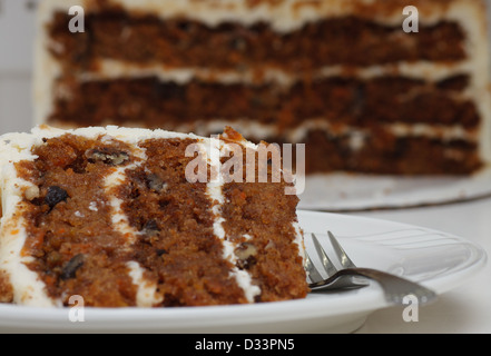 Ein Stück Karottenkuchen auf einem Teller mit einer Gabel einstechen. Halbe Kuchen im Hintergrund Stockfoto