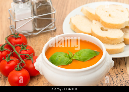 Eine Schüssel mit Tomatensuppe mit frischen Tomaten und auf der Rebe und knusprigem Brot. Stockfoto