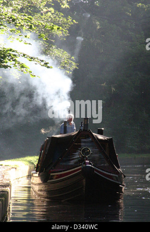 Eine schmale Boot produziert Rauch-Ringe aus dem Auspuff in den frühen Morgenstunden auf der Llangollen Kanal, Wales. Stockfoto