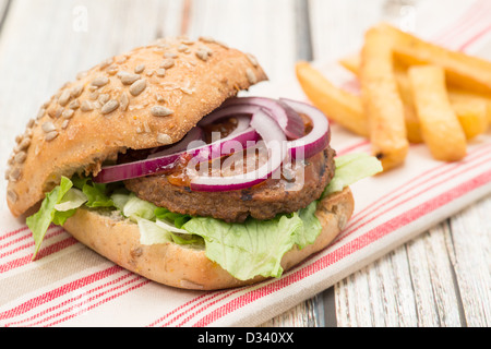 Ein Veggie-Burger mit roten Zwiebeln, Salat und lustvoll in einem Brot Brötchen serviert mit einer Seitenlänge von Pommes frites Stockfoto