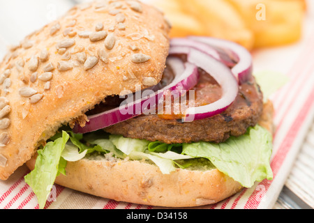 Ein Veggie-Burger mit roten Zwiebeln, Salat und lustvoll in einem Brot Brötchen serviert mit einer Seitenlänge von Pommes frites - geringe Schärfentiefe Stockfoto