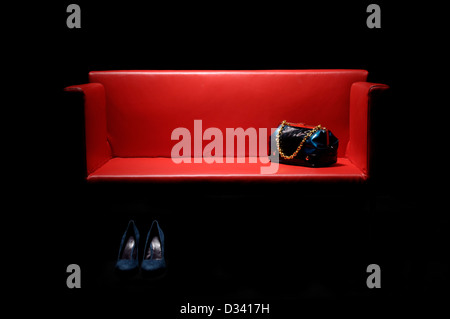 rote Ledercouch mit Handtasche und Damenschuhe. Stockfoto