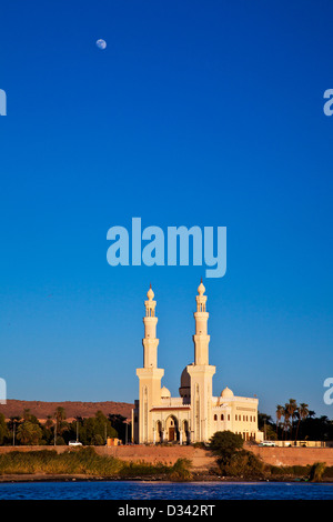 Eine Moschee gebadet im Abendlicht an den Ufern des Nils in der Nähe von Assuan, Ägypten mit dem Mond am blauen Himmel. Stockfoto