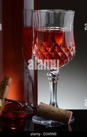 Nahaufnahme von einem geschliffenem Kristallglas Rotwein und eine Flasche gegen eine leichte bis dunkelgrauen Hintergrund. Stockfoto