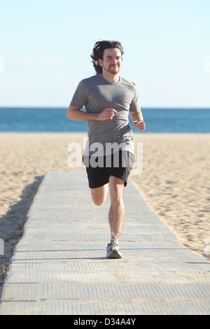 Vorderansicht eines Mannes am Strand mit dem Meer im Hintergrund laufen Stockfoto
