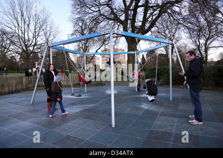 Kinder auf der Schaukel auf Spielplatz in den Lustgärten an der Pittville Pumpe Zimmer Cheltenham Gloucestershire England Stockfoto