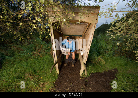 Mann liest The Guardian in einem Outdoor-Toilette. Stockfoto