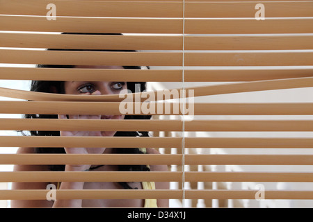 Junge dunkle behaarte Frau hinter einem Fenster Blind, Blick aus dem Fenster. Stockfoto