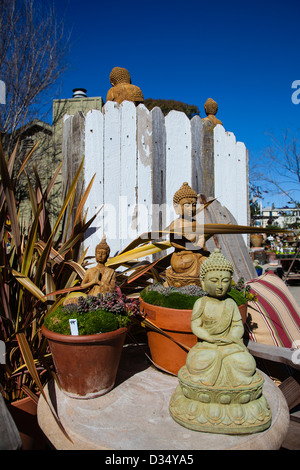 Stein Buddha-Statuen auf dem Display in einem Garten laden befinden sich auf einem Tisch in Blumentöpfe und können über eine hölzerne Trennwand gesehen werden. Stockfoto