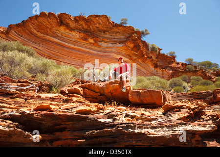 Mann sitzt unten bunt geschichteten Felsen in Schleife zu Fuß, Kalbarri National Park, Western Australia Stockfoto