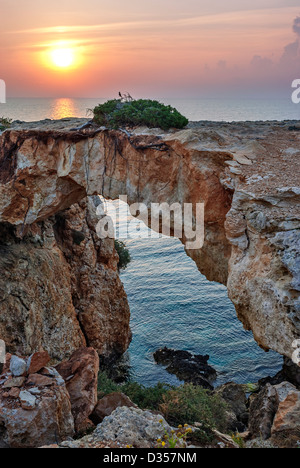 Sonnenuntergang und Steinbogen über Küste auf Zypern Stockfoto