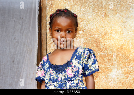 Porträt eines niedlich und süß schwarzen afrikanischen Mädchens, lächelnd, aber auf der Suche nach ein wenig schüchtern, posiert vor ihrem Haus. Stockfoto