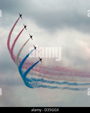 Red Arrows fliegen in Formation zu eine Kurve, mit roten, weißen und blauen Rauch Trails vor einem wolkigen Himmel bilden. Stockfoto