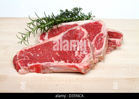 Frische Amerikanische (New York Strip Steak mit Knochen) Rumpsteak auf einem Schneidebrett mit Rosmarin und Tyne Stockfoto