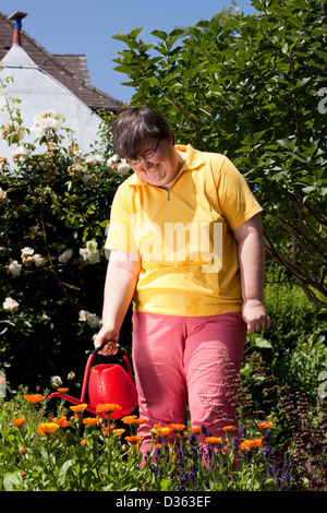 geistig behinderte Frau steht in den Garten und gegossenen Blumen Stockfoto