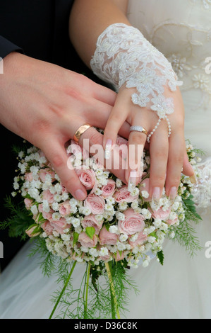 Ein frisch vermählte Paar legen ihre Hände auf einer Hochzeit Bouquet zeigt ihre Eheringe. Stockfoto