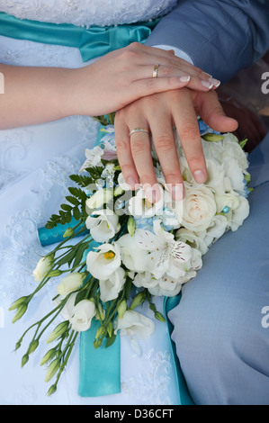 Ein frisch vermählte Paar legen ihre Hände auf einer Hochzeit Bouquet zeigt ihre Eheringe. Stockfoto