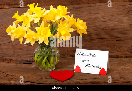 Liebe Grüße zum Muttertag mit einem Bouquet von Narzissen und eine weiße Karte mit dem Text "Alles Liebe Zum Muttertag" Stockfoto