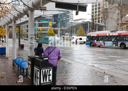 Menschen stehen im Regen warten auf einen Bus am Burrard street downtown Vancouver BC Kanada Stockfoto