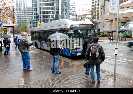Menschen stehen im Regen warten auf einen Bus am Burrard street downtown Vancouver BC Kanada Stockfoto