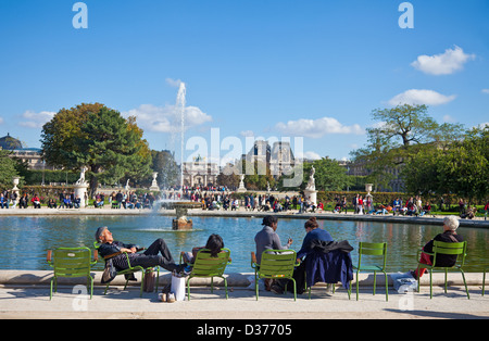 Menschen, die genießen einige Herbstsonne am Rand eines Teiches: Jardin des Tuileries, Paris. Louvre-Museum im Hintergrund. Stockfoto