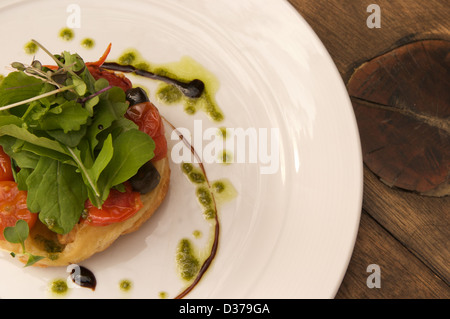Tomaten und Oliven Tarte Tatin mit Rucola-Pesto, Rucola und Balsamico-Sirup serviert auf einem weißen Teller. Stockfoto