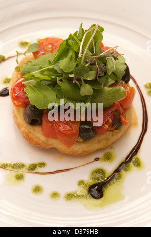 Tomaten und Oliven Tarte Tatin mit Rucola-Pesto, Rucola und Balsamico-Sirup serviert auf einem weißen Teller. Stockfoto