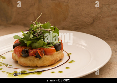 Tomaten und Oliven Tarte Tatin mit Rucola-Pesto, Rucola und Balsamico-Sirup serviert auf einem weißen Teller. Stockfoto