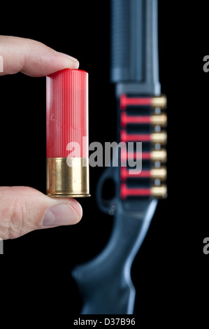 Ein Mann zeigt eine Schrotflinte Shell neben einer Schrotflinte im Hintergrund. Stockfoto