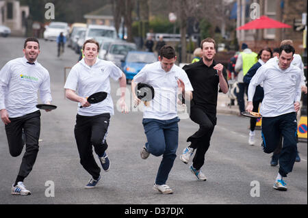 Männliche Konkurrenten (mit Bratpfannen), Laufen oder Rennen in traditionellen, Ilkley Rotary Pancake Race - The Grove, Ilkley, West Yorkshire, UK. Stockfoto