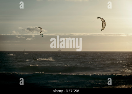 Zwei Kite-Surfer genießen die letzten Surf des Tages als eine Ladung Schiff Durchläufe im Hintergrund auf Blouberg Strand. Stockfoto